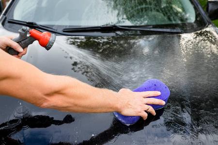 手特写与紫色刷洗黑色汽车洗车的概念. 男人用海绵和肥皂洗自己的车.