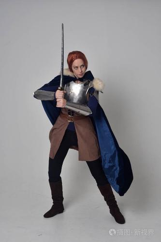 一个穿着中世纪战士服装,蓝色天鹅绒斗篷和钢甲站立姿势的红头发女孩