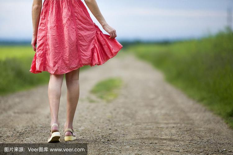背影的年轻女子在红色的裙子腿走在地面道路上在夏天的一天模糊的阳光