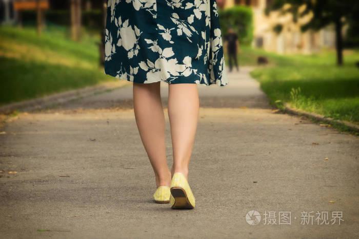 女孩穿着黄色的鞋子在公园里散步. 女孩的腿从后面.