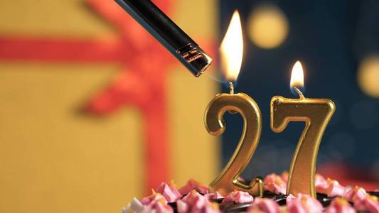 生日蛋糕27号,打火机点燃金色蜡烛,背景礼物黄色盒子系上红丝带.