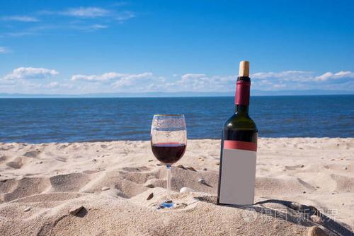 一杯红酒和一瓶在一个阳光明媚的夏日的海滩上.在背景中的大海和蓝天